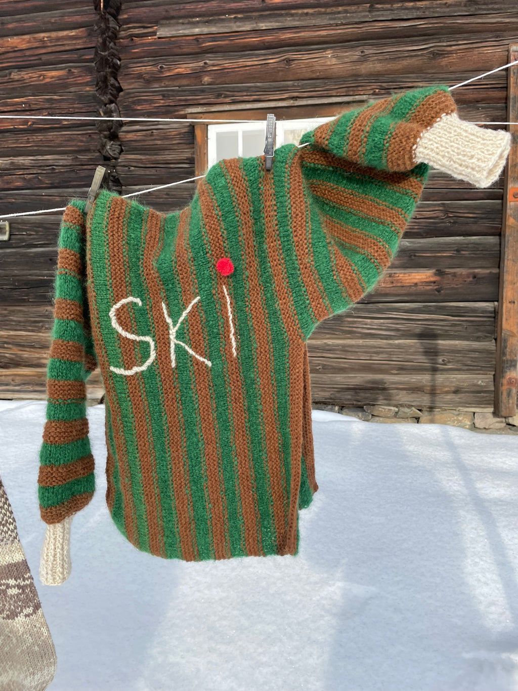 Genser med grønne og brune striper, voluminøse puffermer og sidesplitt – Ski Inn, Ski Out fra CosyMonday