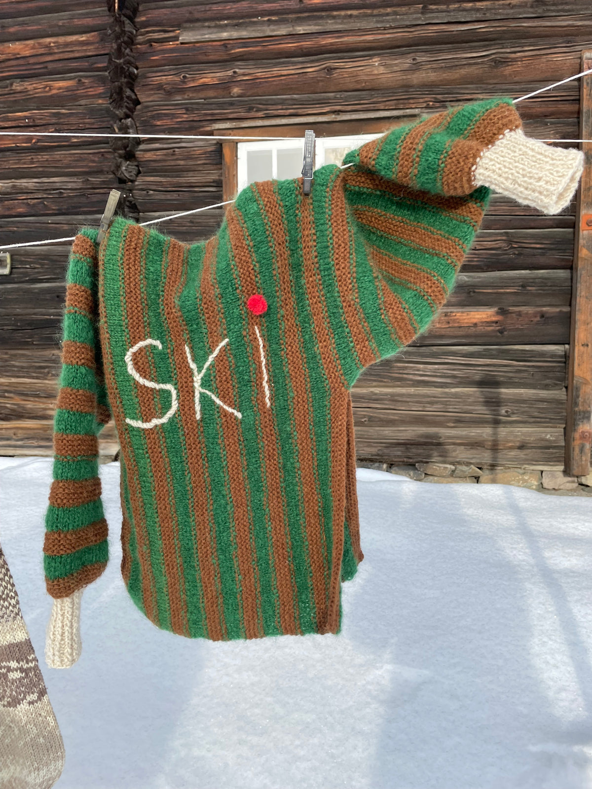 Genser med grønne og brune striper, voluminøse puffermer og sidesplitt – Ski Inn, Ski Out fra CosyMonday